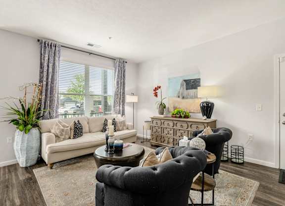A living room with a grey armchair, a white sofa, a wooden coffee table, and a white vase with a green plant.