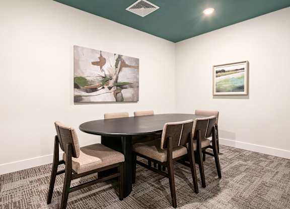 A conference room with a table and chairs and two pictures on the wall.