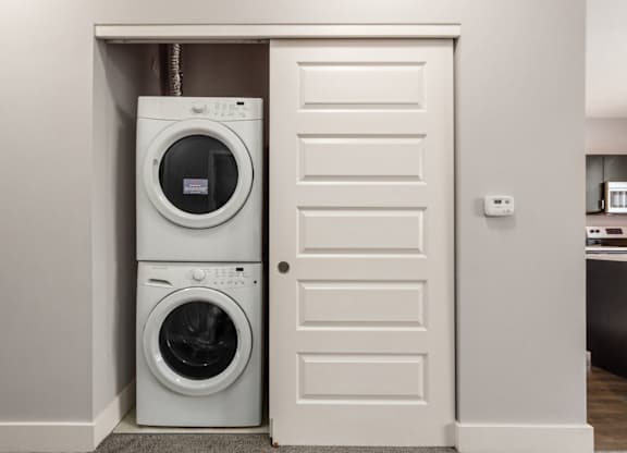 A white door is open to reveal a stacked washer and dryer.