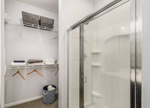 A bathroom with a white shower stall and a white towel rack with towels hanging on it.