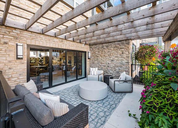 A patio with a black sofa, a round table and a stone wall.