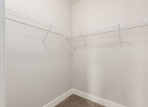 A white closet with a carpeted floor and a white wall.