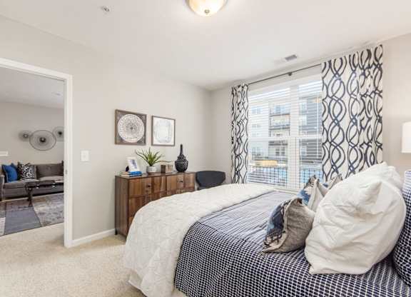 A bedroom with a bed, nightstand, and a window with a view of a building outside.