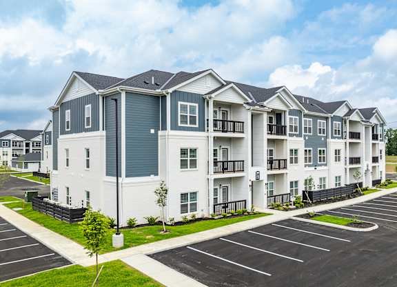 A large white and grey apartment complex with a parking lot in front.