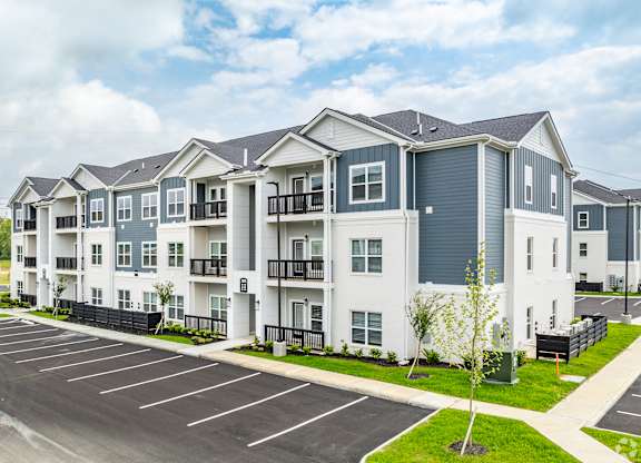 A large white apartment building with a parking lot in front.