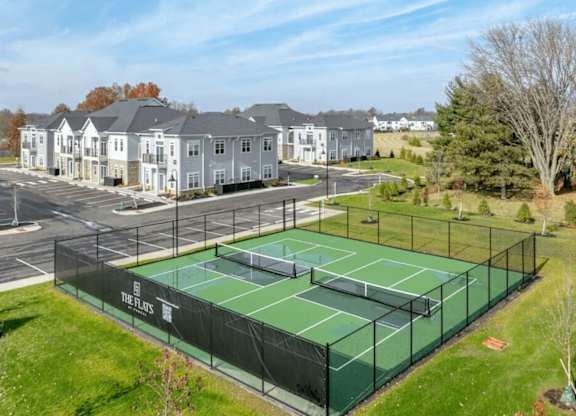 A tennis court is surrounded by a fence and apartment buildings.
