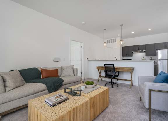A living room with a couch, a coffee table, and a kitchen area in the background.