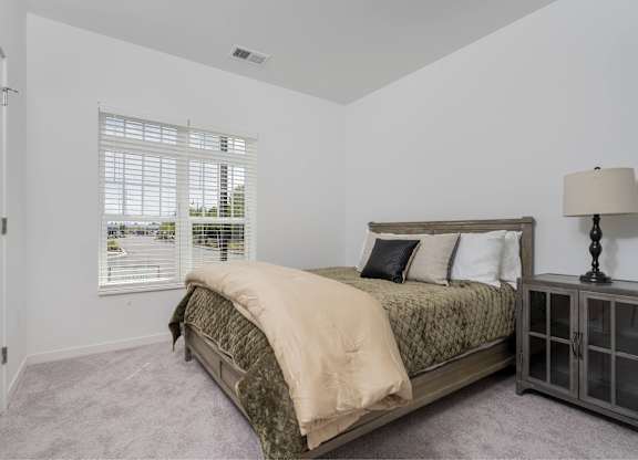 A bedroom with a bed, nightstand, and window with blinds.