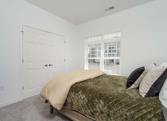 A bed with a green blanket and two pillows sits in a room with a window.