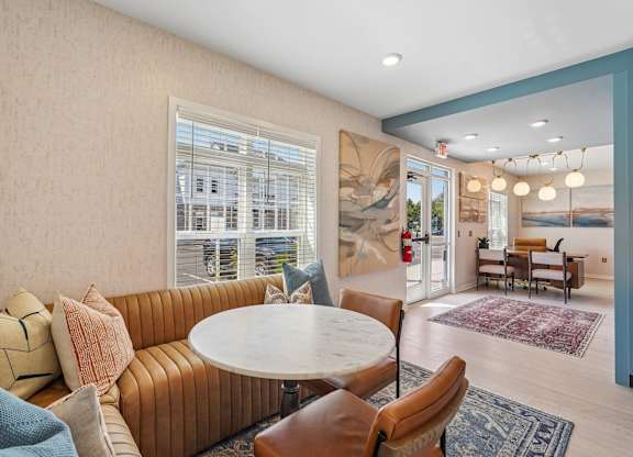 A living room with a round table surrounded by chairs and a large window.