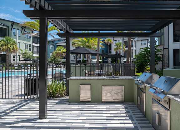A patio area with a grill and a pool in the background.