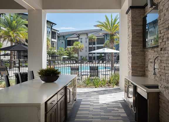 A kitchen with a view of a pool and palm trees.