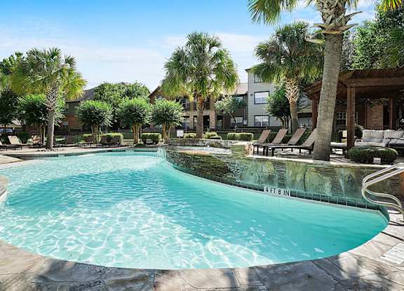 A swimming pool surrounded by palm trees and lounge chairs.