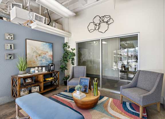 A modern living room with a grey sofa, a grey armchair, a wooden coffee table, and a large painting on the wall.