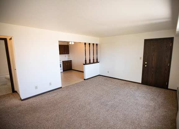 A large empty room with a carpeted floor and a door on the right side.