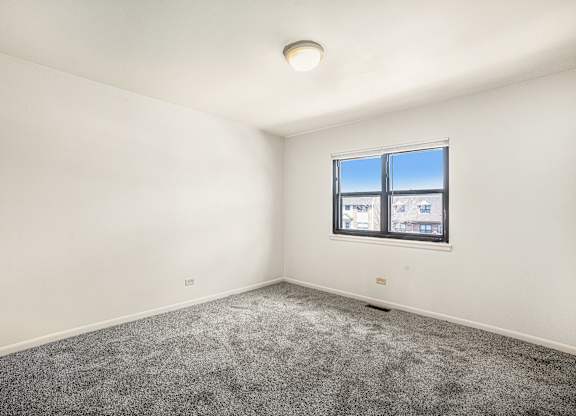 A room with a window and a grey carpet.