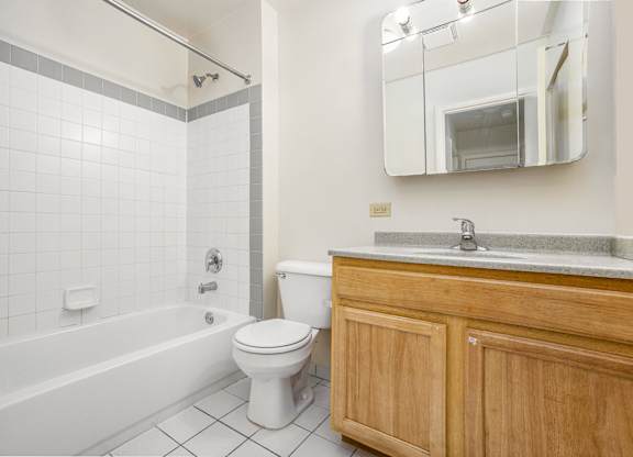 A white tiled bathroom with a wooden cabinet and a white toilet.