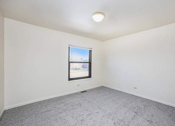 A room with a window and a grey carpet.