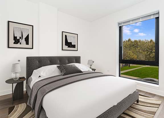 A bedroom with a large bed and a view of a green lawn outside the window.