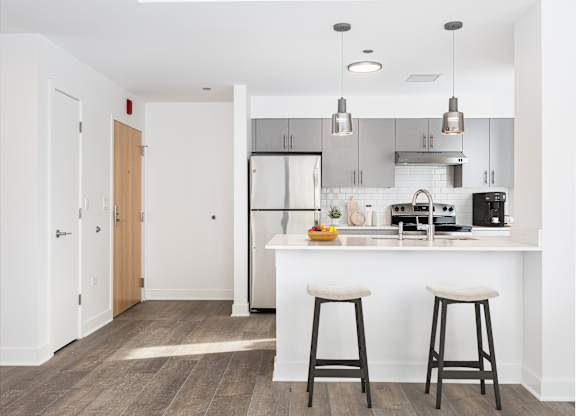 A kitchen with white countertops and bar stools.