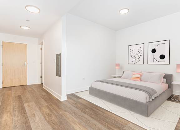 A bedroom with a bed, two pictures on the wall, and a wooden floor.