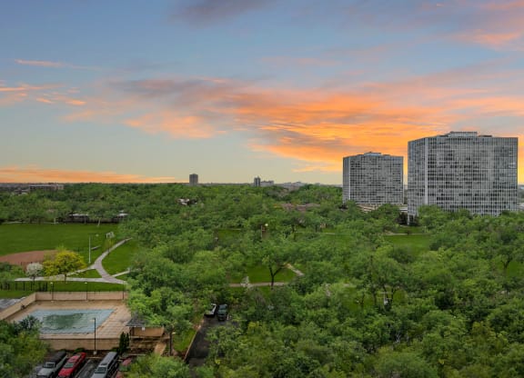 an aerial view of a park with buildings in the background and a colorful sunset in the sky at The Pavilion, Detroit, MI, 48207