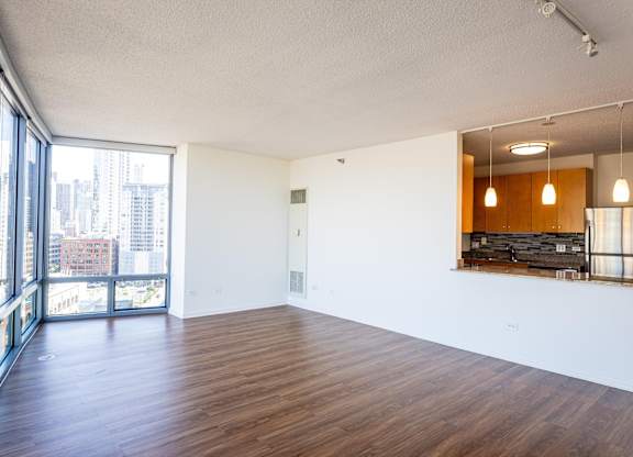 A large empty room with wooden floors and a view of the city through the windows.
