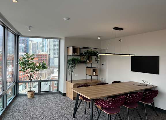 A conference room with a long table and chairs, a flat screen TV, and a view of the city outside the window at Kingsbury Plaza, Chicago, 60654