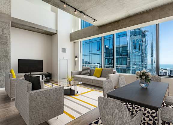 A modern living room with a grey sofa, a black coffee table, and a large window overlooking the city.