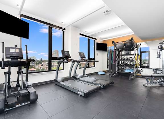 a gym with cardio equipment and windows with a view of the city