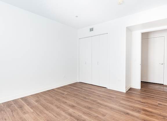 A room with white walls and wooden flooring with two white doors.