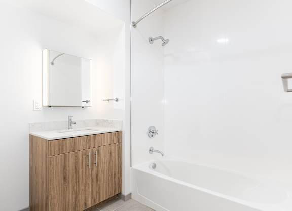 A white bathroom with a wooden cabinet and a white tub.