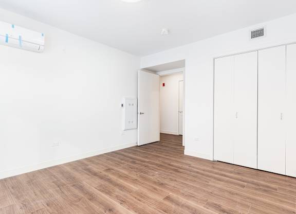 A room with white walls and wooden flooring, featuring a white door and a white cabinet.