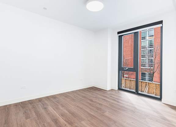 A room with a wooden floor and a window with a view of a building outside.