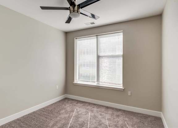 A room with a ceiling fan and a window with blinds.