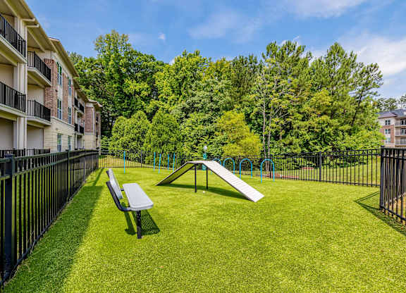 A park with a slide and bench in the foreground and apartment buildings in the background. at 1701 North Apartment Homes Apartments, Chapel Hill, NC