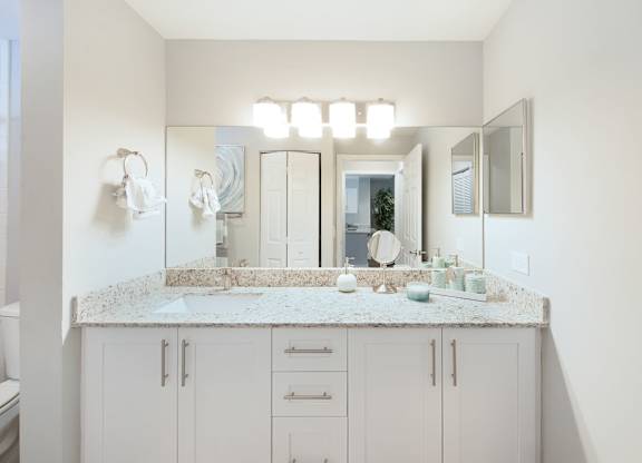 A bathroom with a marble countertop and white cabinets.