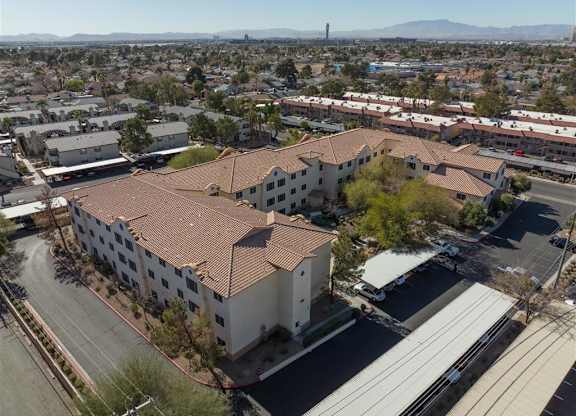 A large white building with a red tile roof is surrounded by a parking lot and other buildings.