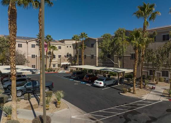 A parking lot with cars and palm trees in front of a building.