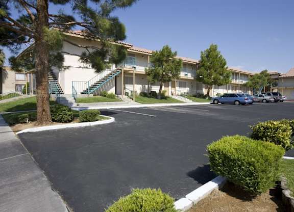 A parking lot in front of a building with a tree and bushes.