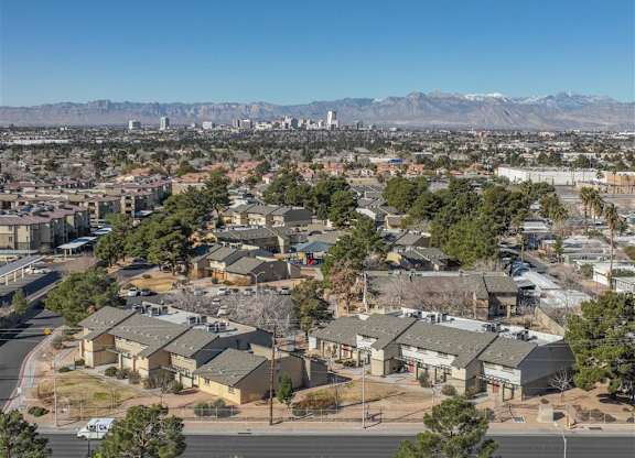 A residential area with houses and trees in the foreground and a city skyline with mountains in the background.