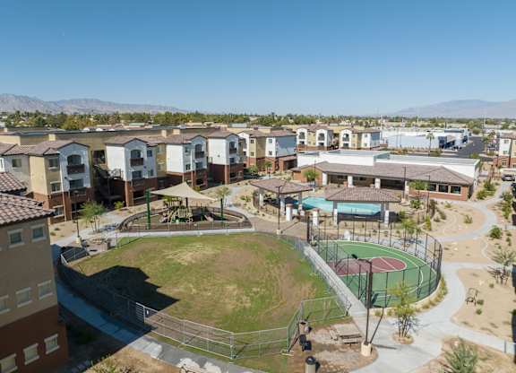 A park with a basketball court and a playground is surrounded by apartment buildings.