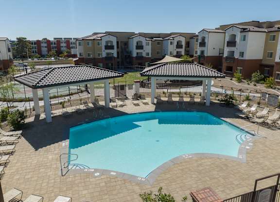 A swimming pool surrounded by a patio and gazebo in a residential area.