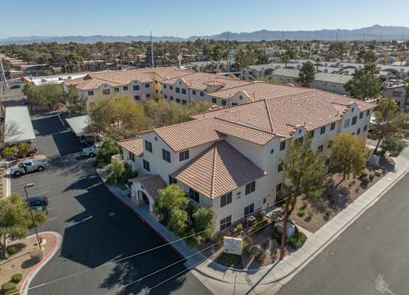 A large white building with a red roof is surrounded by a parking lot.