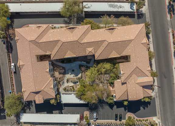 A large building with a brown roof is surrounded by trees and a parking lot.