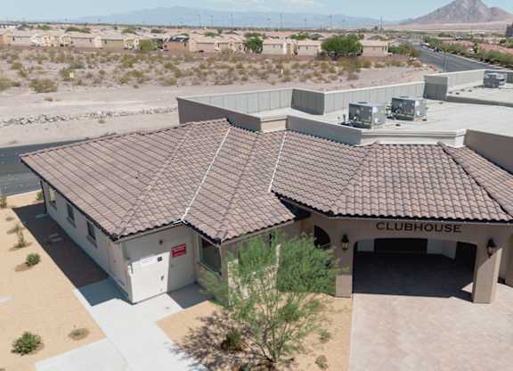 A clubhouse with a brown roof is surrounded by a parking lot and other buildings.