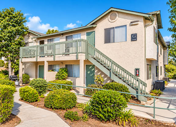 A beige building with a green railing and bushes in front.