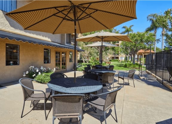 a patio with tables and umbrellas in front of a building at Huntington Terrace North Senior, Huntington Beach, CA
