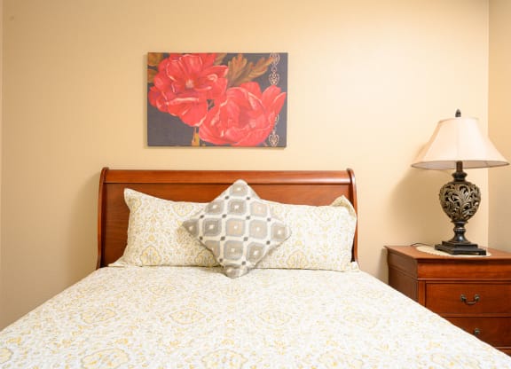 a bedroom with a bed and a nightstand with a lamp at Oak Terrace Senior Apts, Hemet, CA 92543