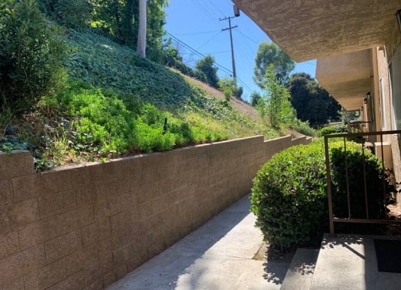 a patio with a retaining wall and bushes on the side of a house at North View Terrace, Montebello